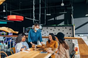 A waitress with a protective mask on her face brings the restaurant guests the meal they ordered.