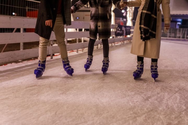 Three friends holding hands and ice skating together at the ice rink