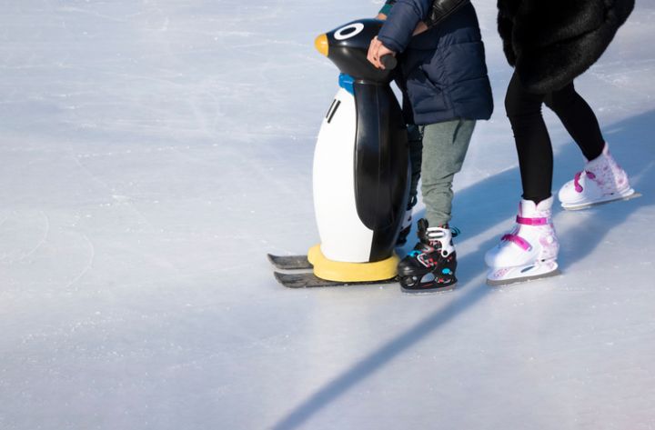 Ice rink. Mom teaches a child to skate. A boy holds a penguin for support. Winter family activities and sport concept